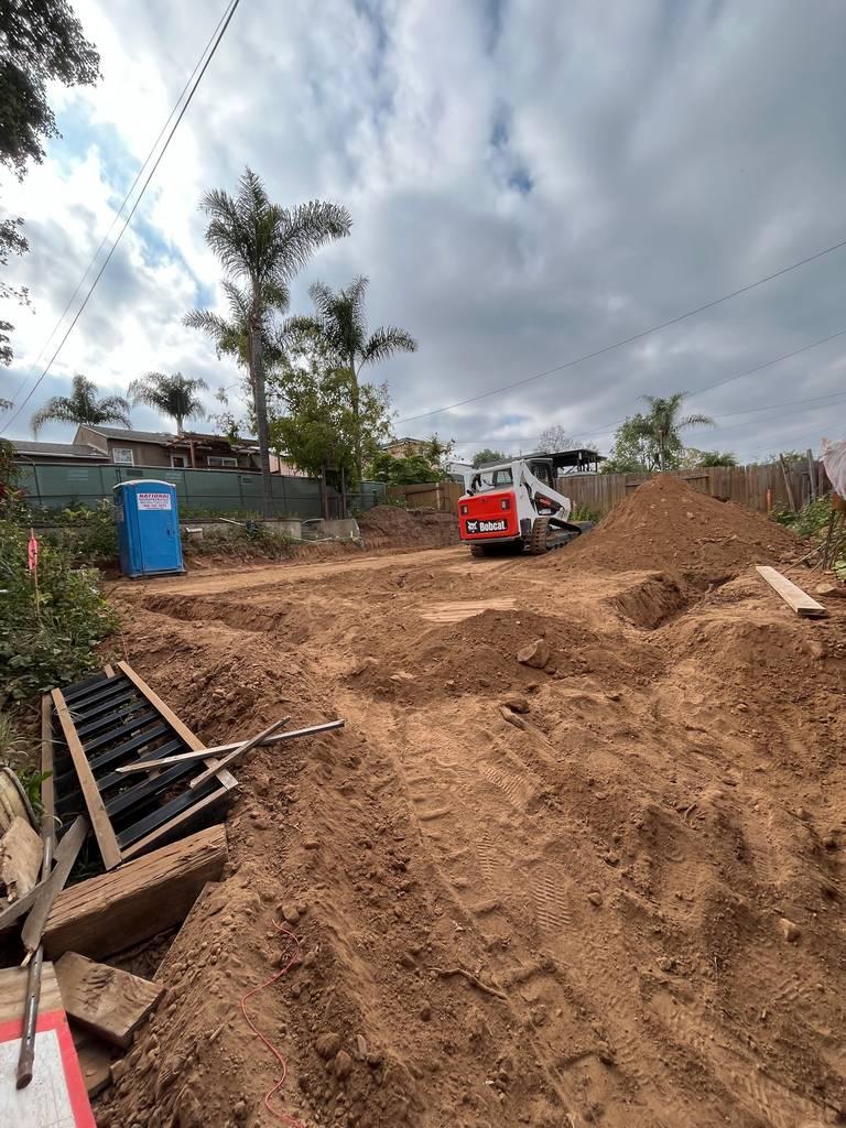 Wide view of job site showing earthwork and Bobcat grading.