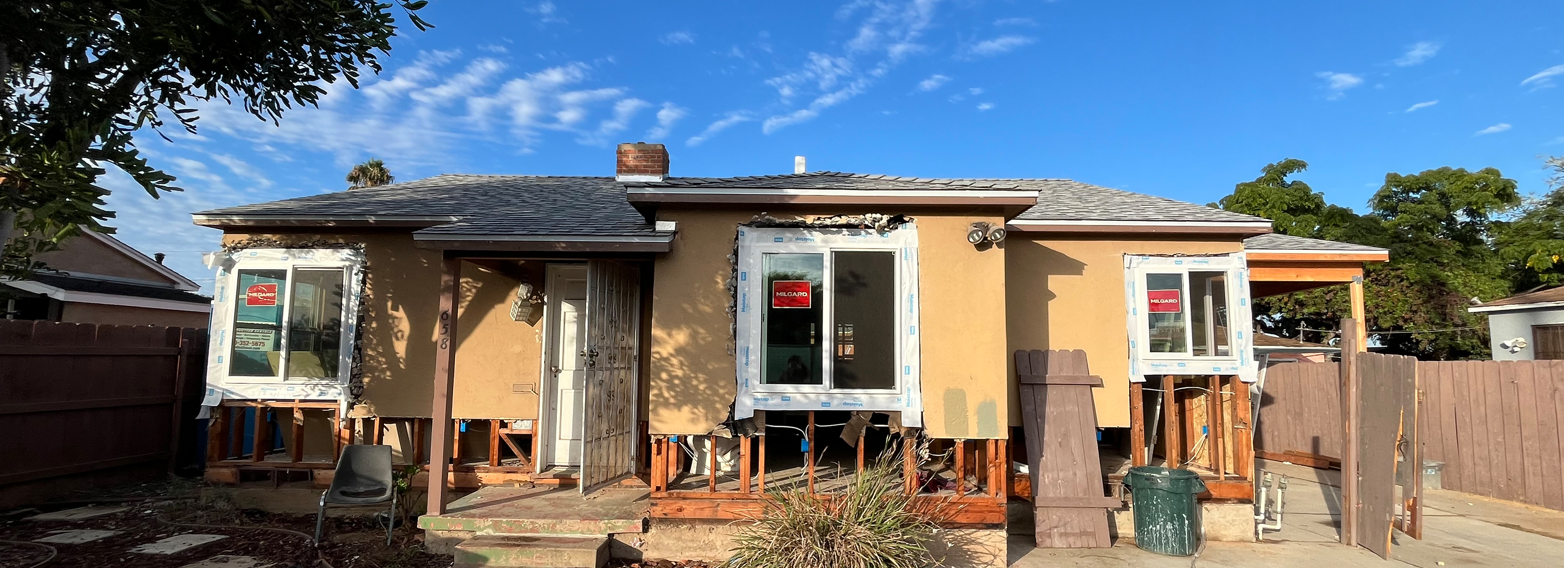 Panoramic exterior view showing window installs and open framing during siding replacement prep.