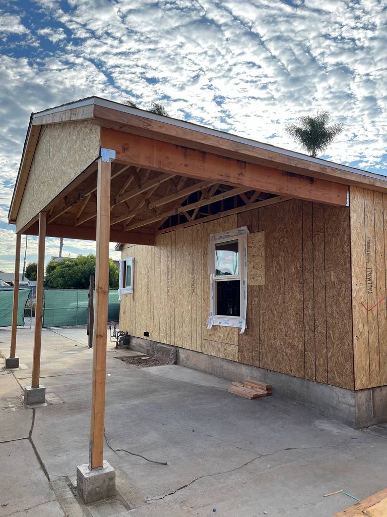 Residential exterior showing front elevation progress with windows installed and framing prepared for new siding.