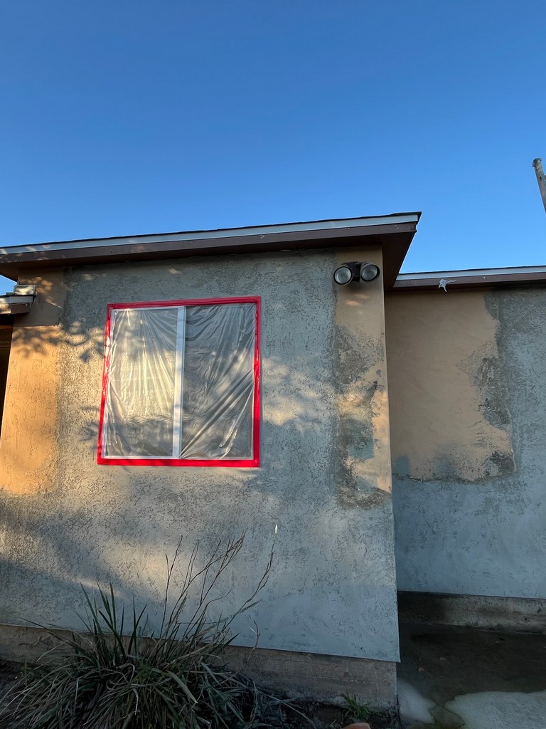 Exterior stucco wall with window masked for surface preparation and coating.