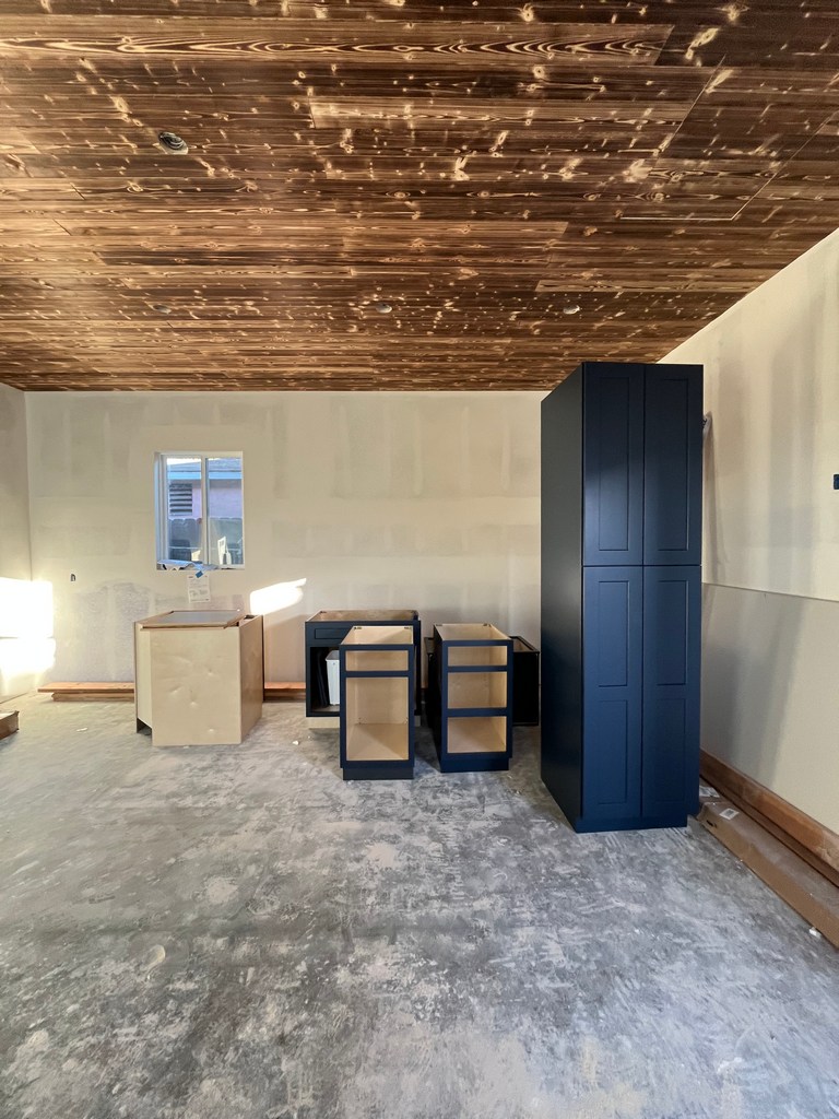 Kitchen cabinet installation beneath wood plank ceiling in residential interior remodel.