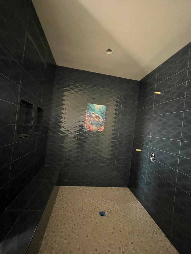 ustom tiled shower with dark wall tile, decorative inlay, recessed niches.