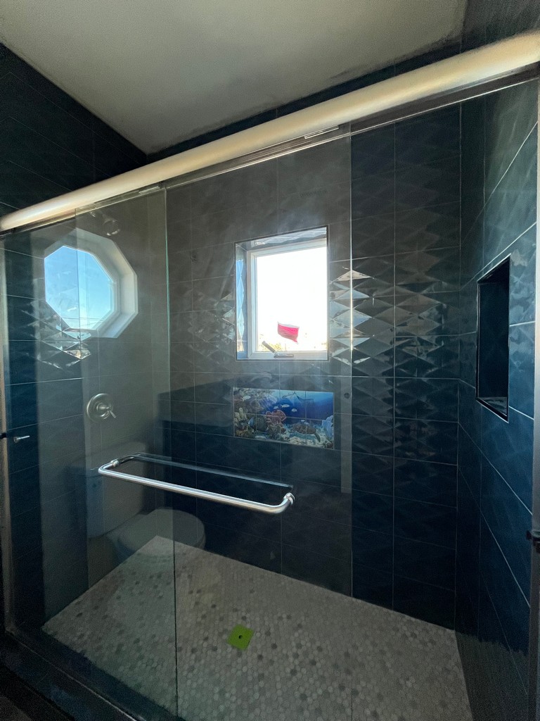 Shower enclosure with installed glass panel, grab bar, tiled walls, and finished shower pan.