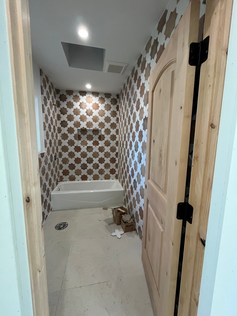 bathroom view showing tub installed with patterned tile, recessed niche, and ceiling lighting