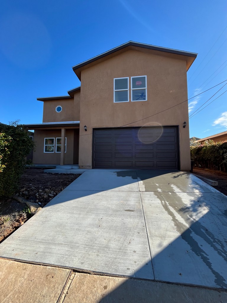Front exterior elevation with finished stucco, new garage door, and poured concrete driveway.