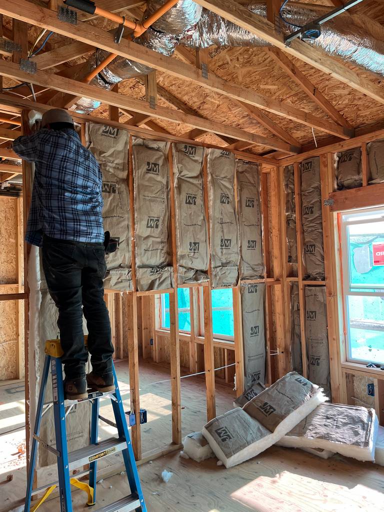 Installer on ladder placing batt insulation in ceiling framing.