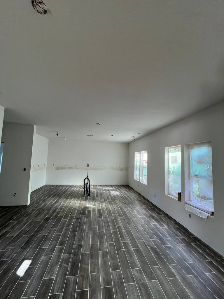 Large living space with wood-look tile flooring and primed walls, ready for finish work.