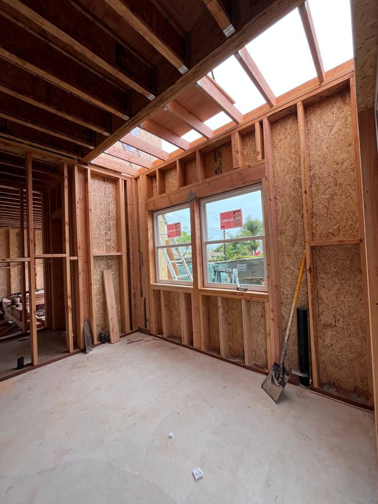 Interior framing with exposed ceiling joists and newly installed dual windows, showing roof cutout for skylight or ventilation.