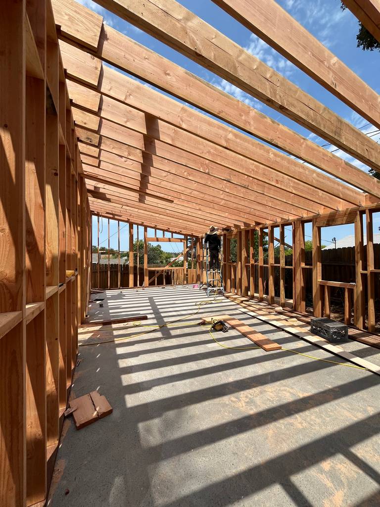 Wide shot shows full interior framing layout with wall studs and exposed ceiling joists