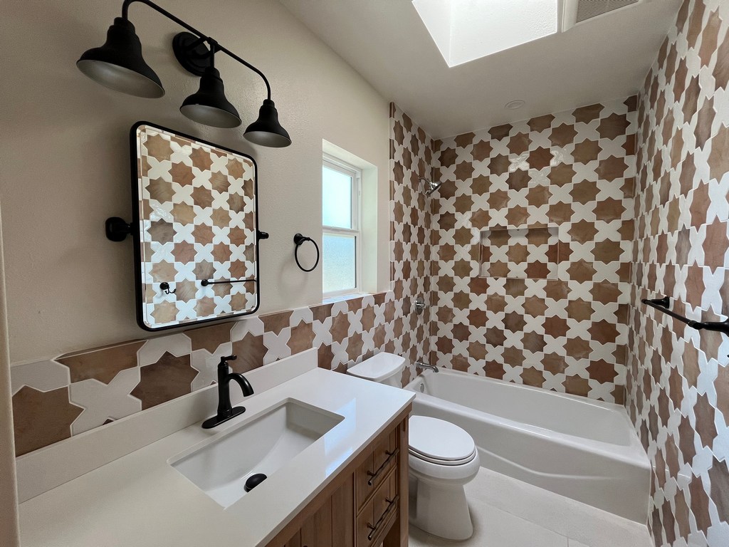 Finished bathroom featuring wood vanity, modern lighting, and full-wall geometric tile.