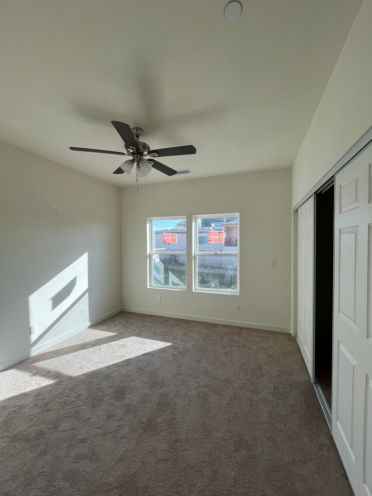 Bedroom with ceiling fan, windows, and finished carpet flooring.