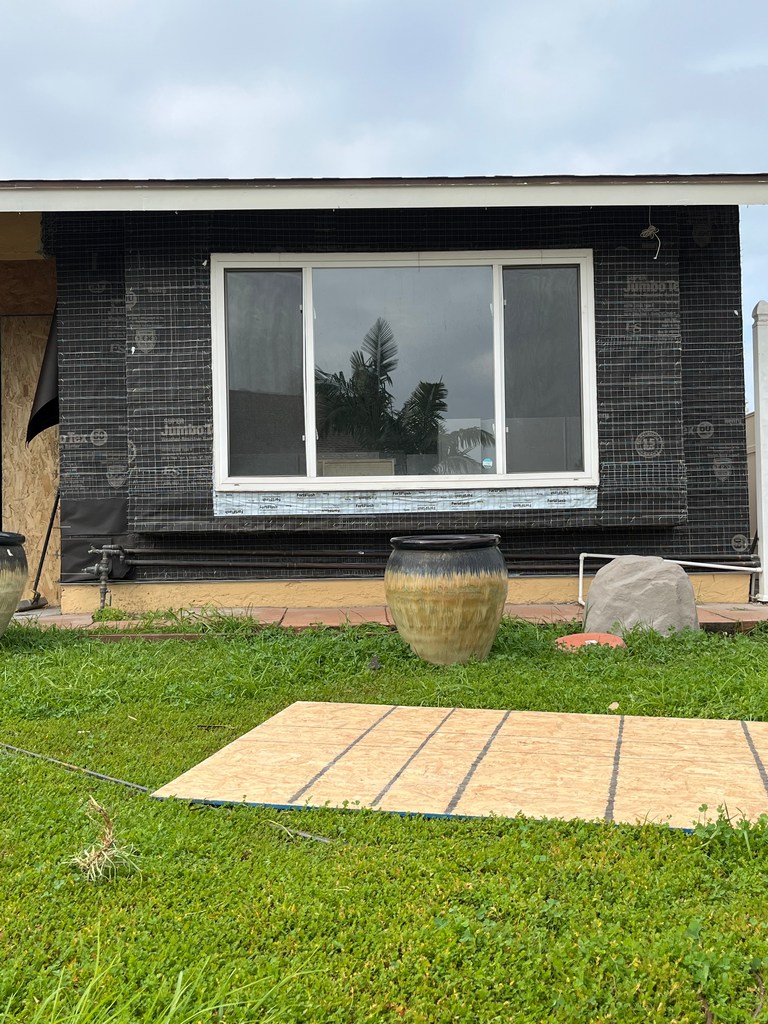 Exterior wall wrapped with weather barrier and stucco lath around a new window opening.