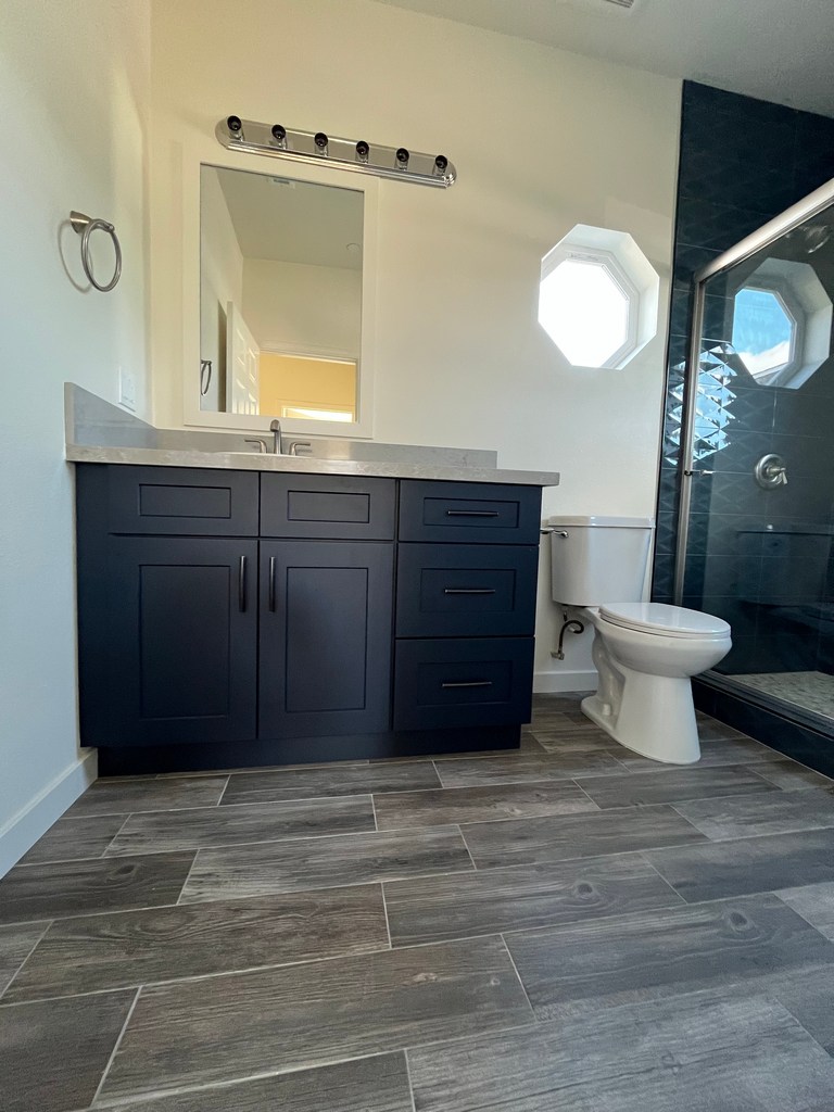 Bathroom vanity and toilet with plank tile floor.