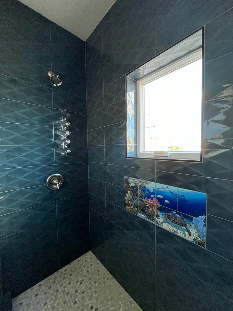 Tiled shower close-up featuring window surround, textured wall tile, ocean accent.