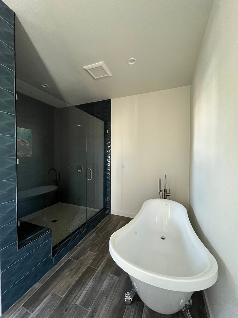 Bathroom showing tiled shower, toilet placement, vanity cabinet, and finished plank flooring