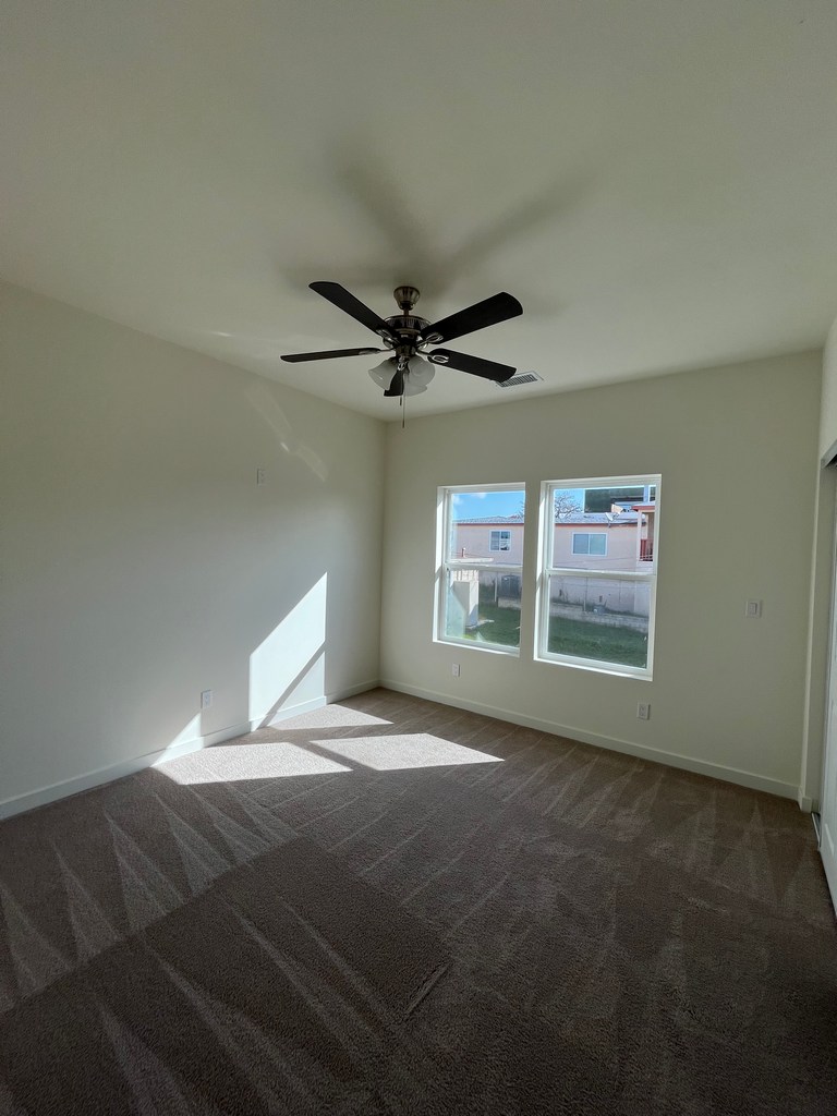 Bedroom corner view featuring carpet flooring, ceiling fan fixture.