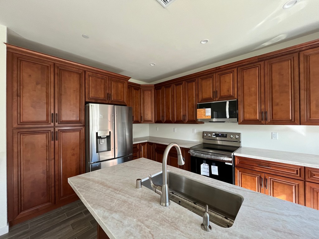 Kitchen showing full-height wood cabinets, stainless range and refrigerator, and quartz countertops.