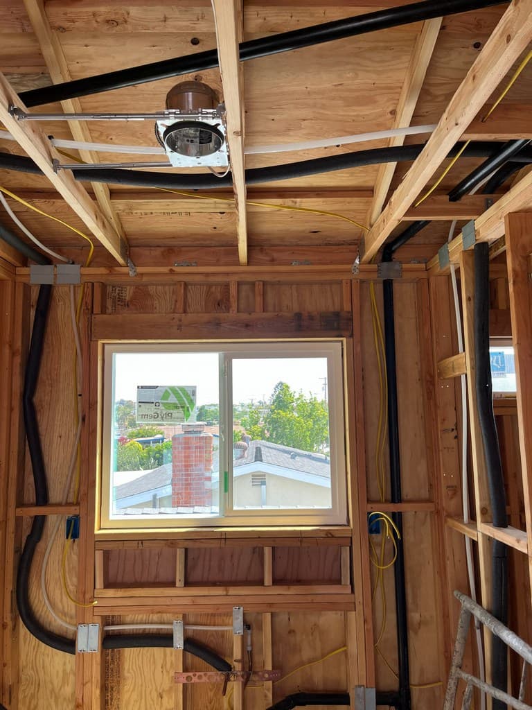 Window wall framing shows plumbing and electrical rough-in around the new ADU living space.