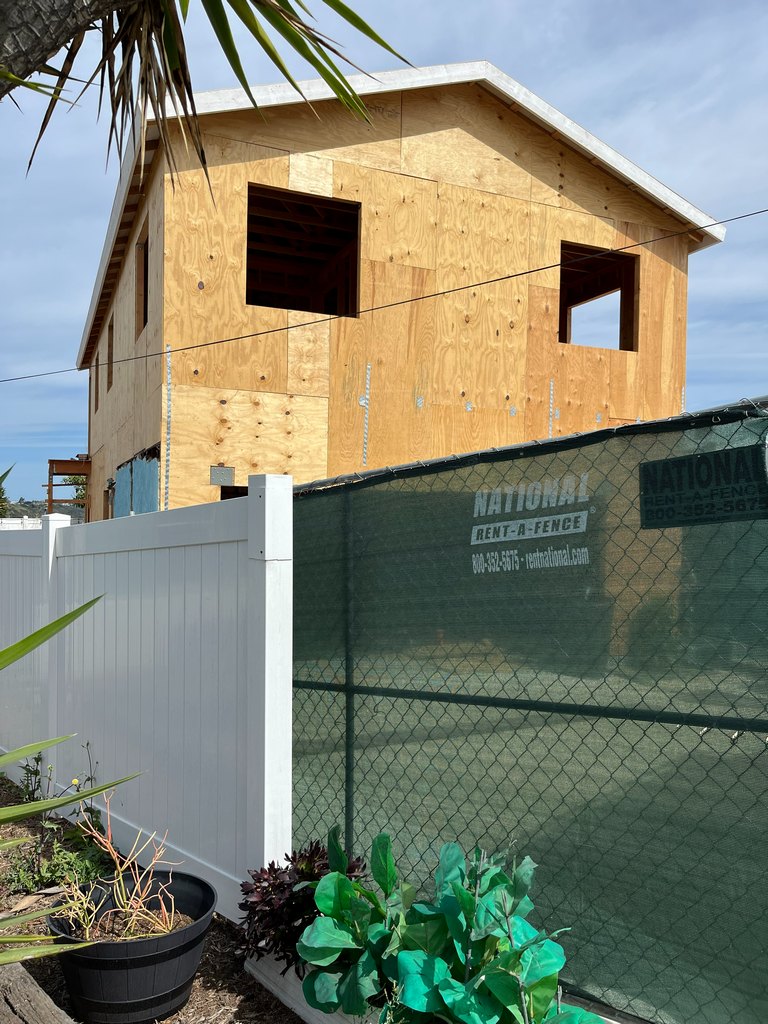 construction fence showing plywood wall sheathing, two framed upper-level windows