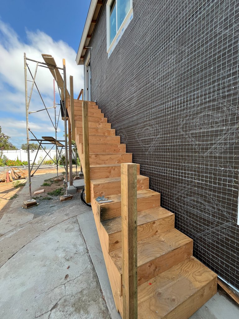 unfinished exterior wood staircase running along the lath-covered guest house