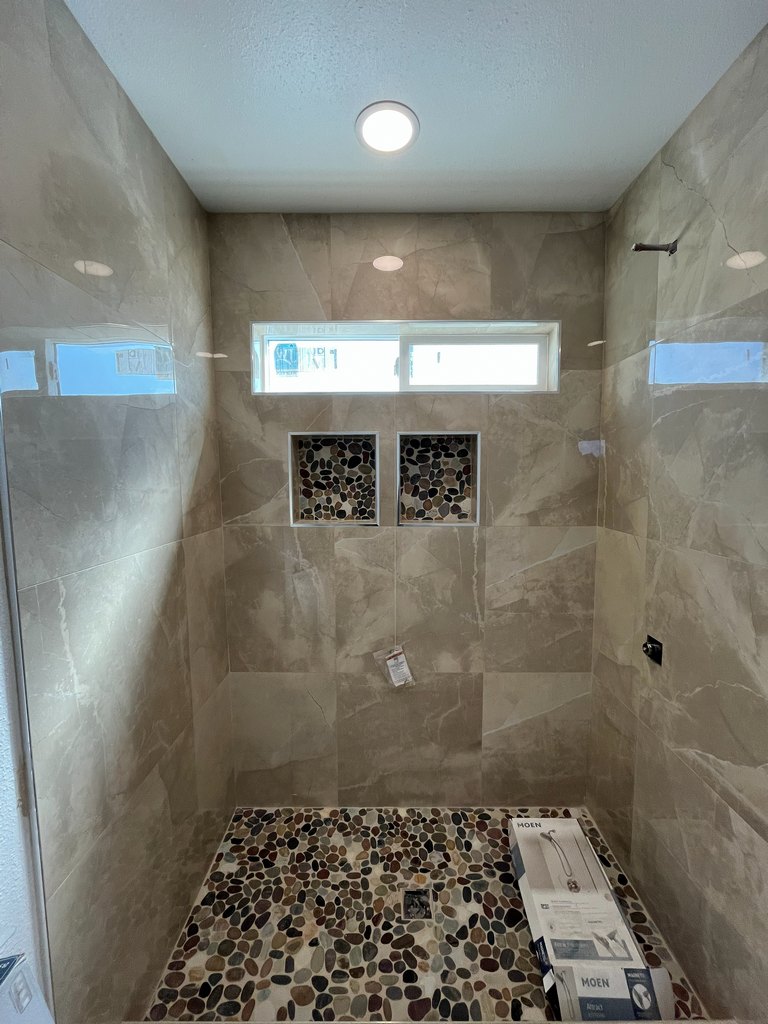 shower featuring large-format wall tile, a pebble-mosaic floor and matching niches