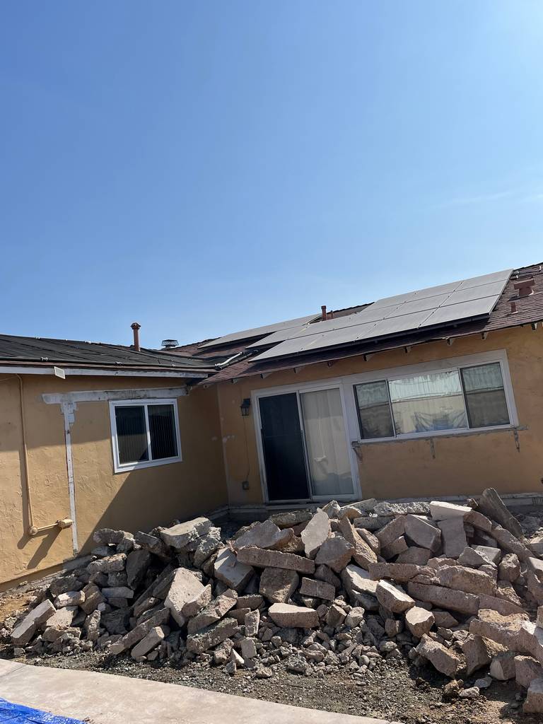 Backyard demolition showing broken concrete slab piled near the house exterior wall.