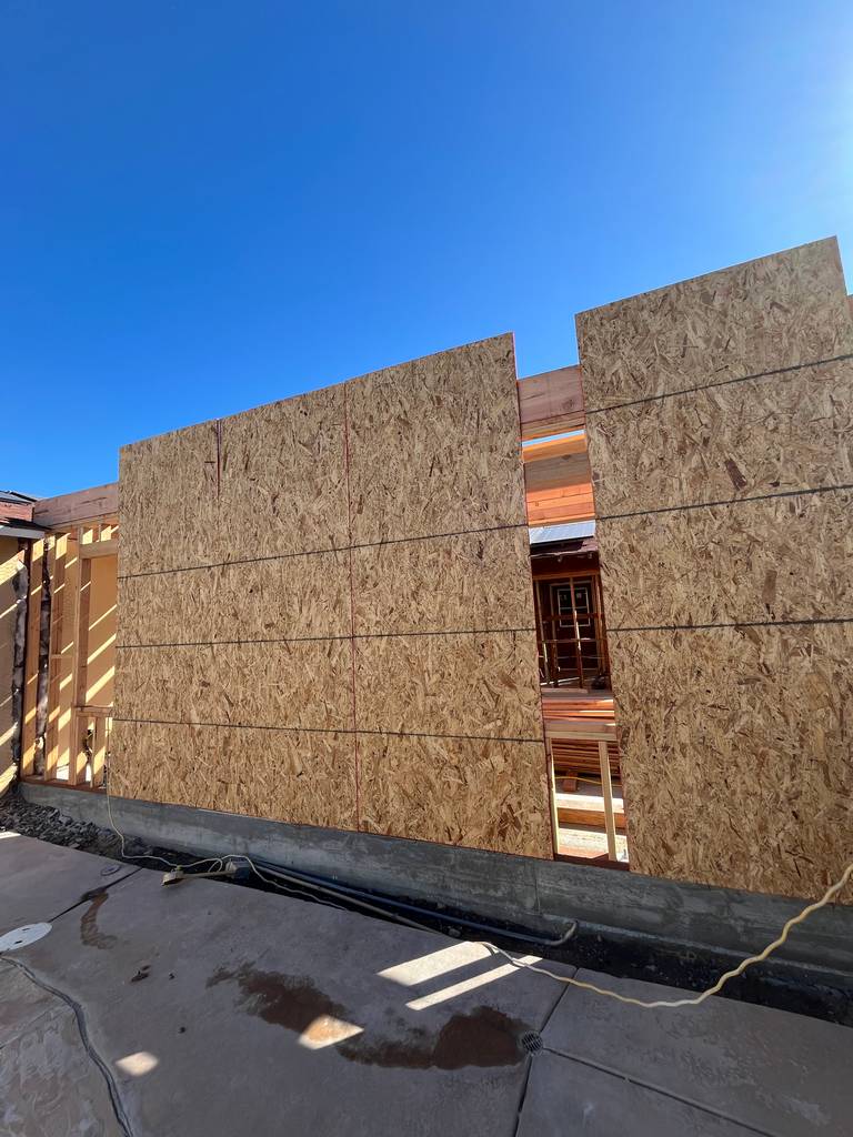 Exterior wall sheathing in progress showing vertical framing alignment and open top section.
