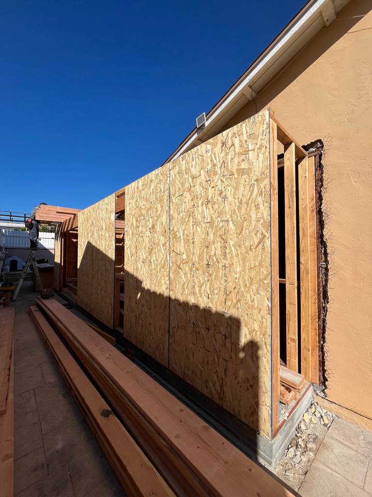 Side view of newly framed and sheathed exterior wall with stacked lumber ready for installation.