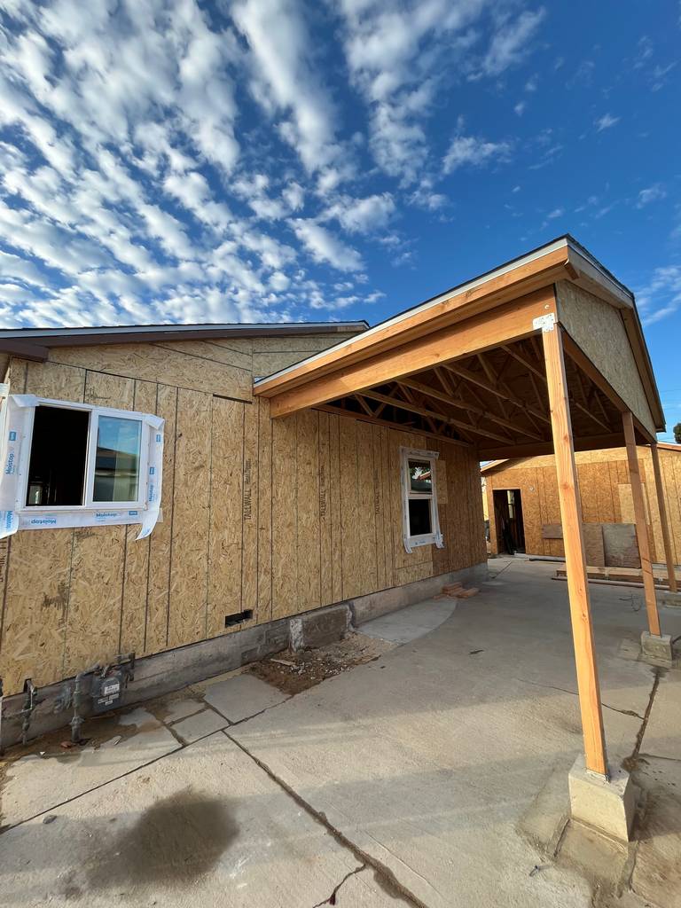 Residential exterior showing front elevation progress with windows installed and framing prepared for new siding.