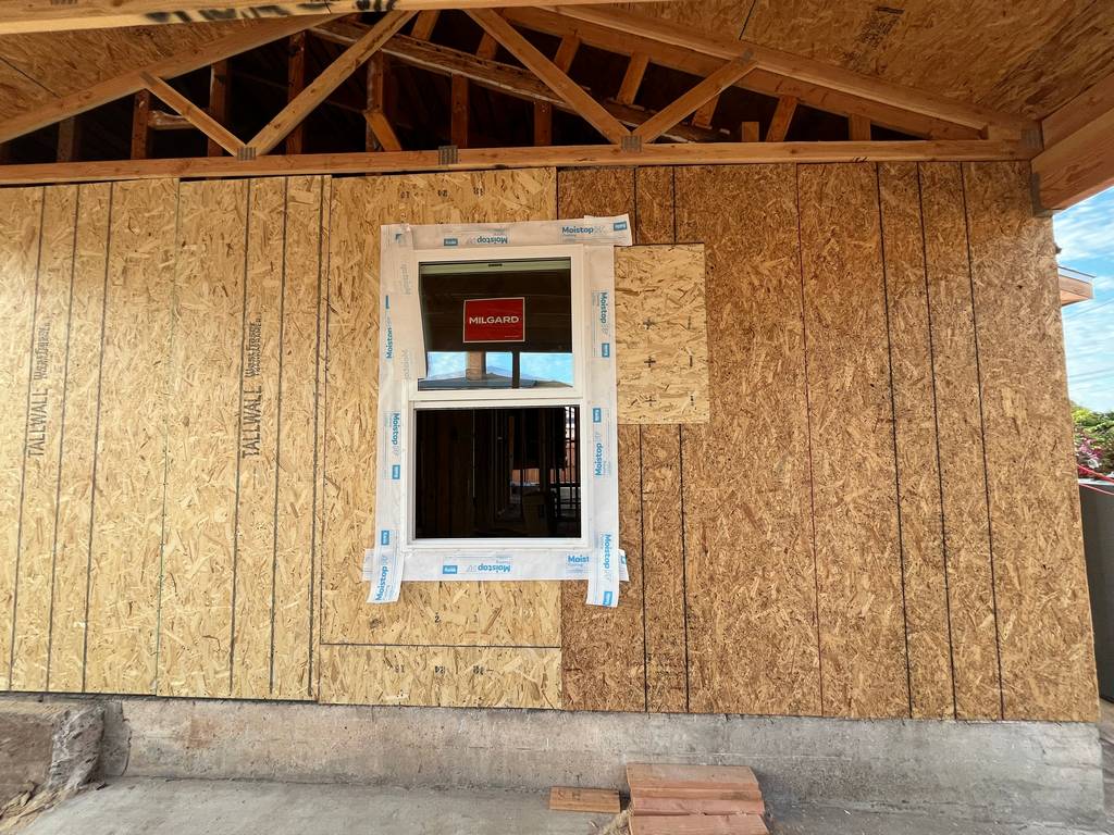 Residential exterior showing front elevation progress with windows installed and framing prepared for new siding.