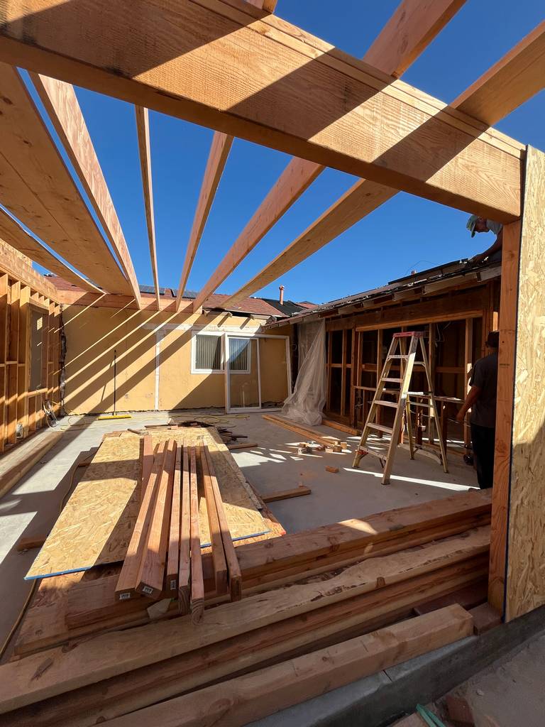 Roof joists installation over open patio area with lumber staged for build.