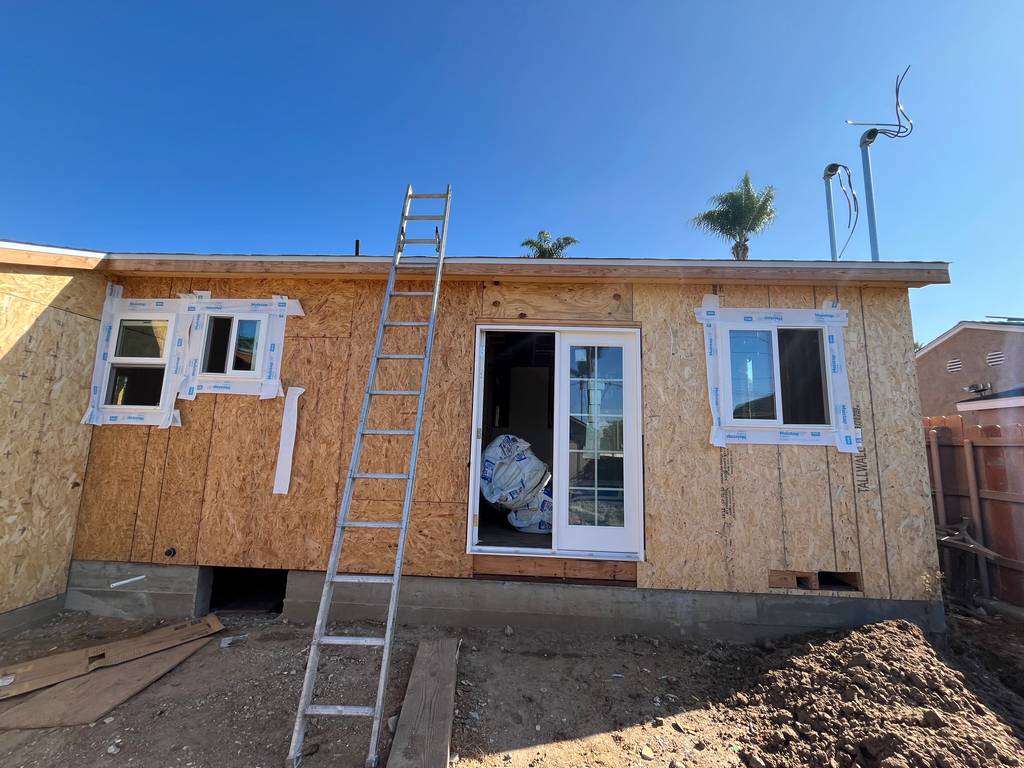 Exterior wall sheathed with new window frames installed and door opening prepped.