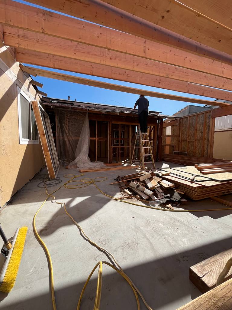 Crew member working on roof framing from ladder under newly set joists.