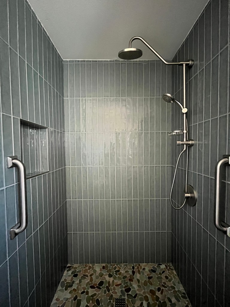 Close-up view of a completed gray vertical tile walk-in shower with pebble stone shower floor