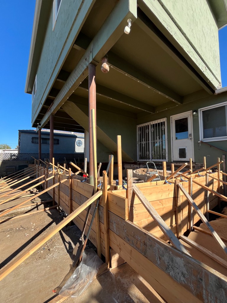 Formwork installation beneath existing structure showing layout around support columns and footing preparation.