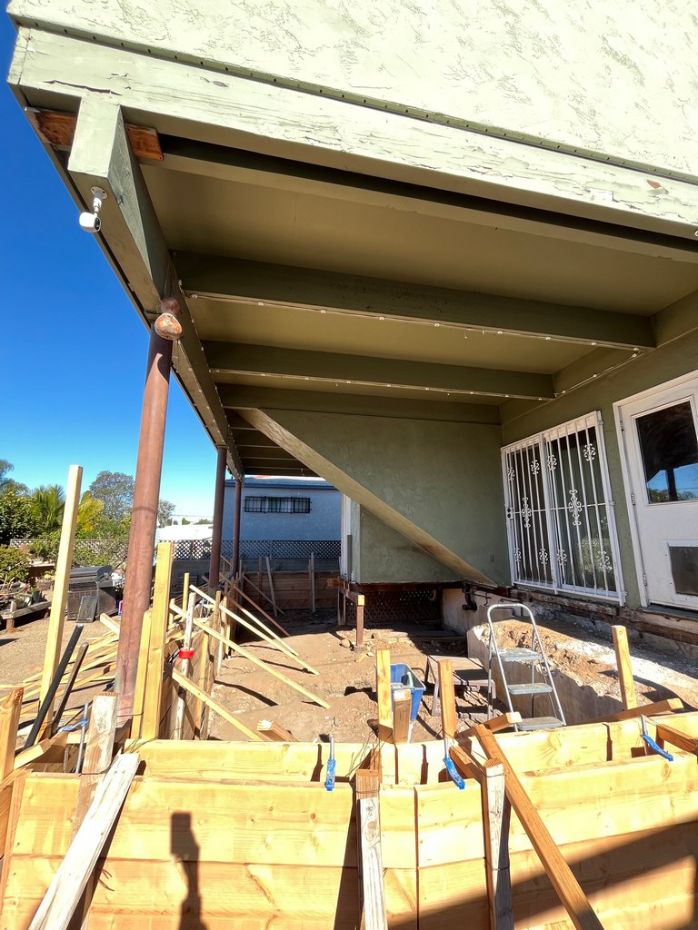 Foundation preparation under existing structure showing excavation and formwork setup for new addition.
