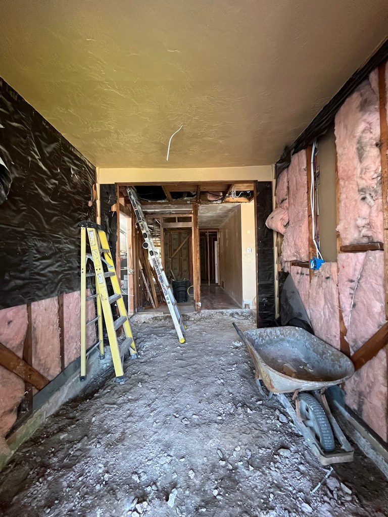 Interior demolition debris and exposed framing with insulation staged for cleanup and rebuild.