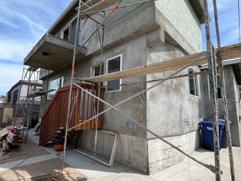 Stucco application in progress on exterior addition walls with scaffolding setup for finishing work.