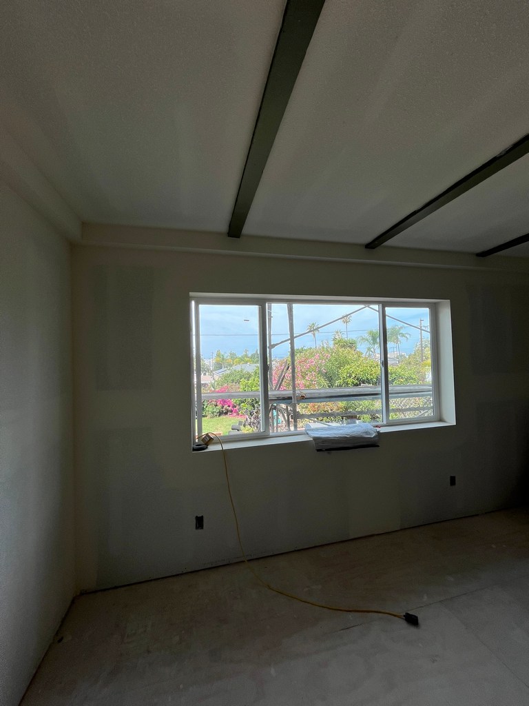 Interior room showing installed window, finished drywall, and preparation for flooring and trim work.