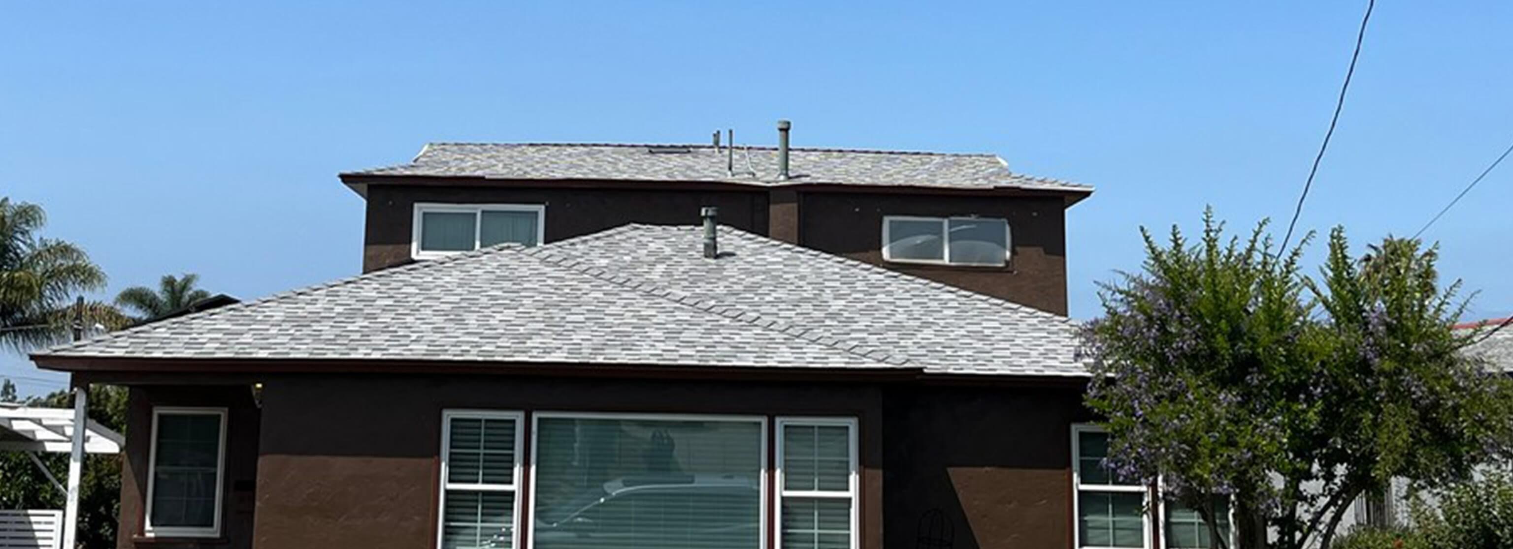 Residential exterior with gray shingle roof, stucco walls, windows, and roof vents.
