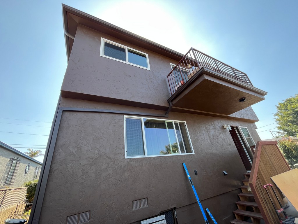 Rear stucco elevation with balcony, windows, stairs, and exterior trim details.