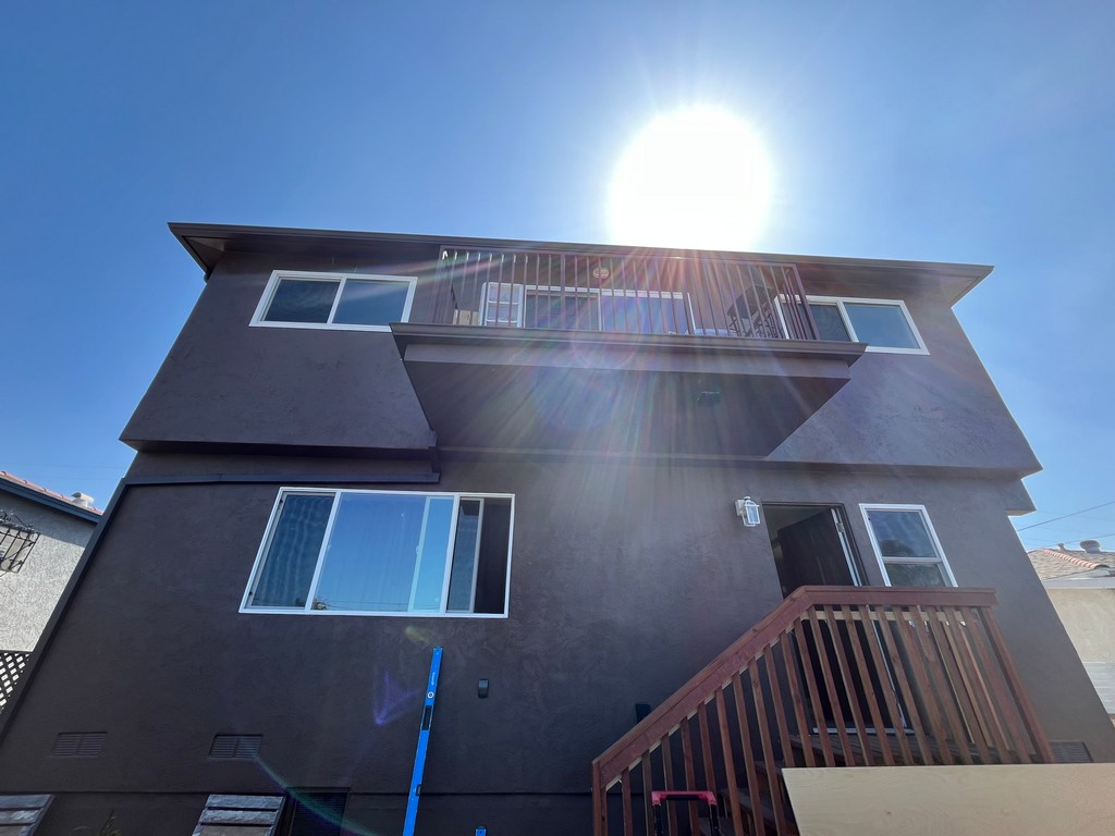 Rear two-story stucco wall with balcony, windows, stairs, and roofline.