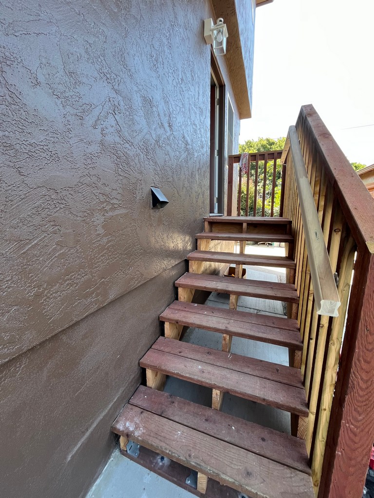 Exterior stair access beside textured stucco wall, wood railing, and residential entry.