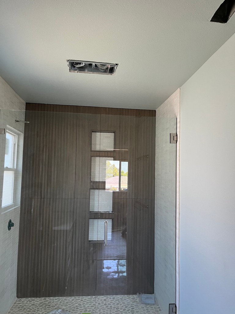 Bathroom shower with glass enclosure, vertical wall tile, pebble floor, and ceiling opening.