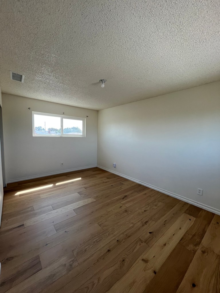 Finished room with hardwood flooring, painted walls, baseboards, window, and ceiling fixture.