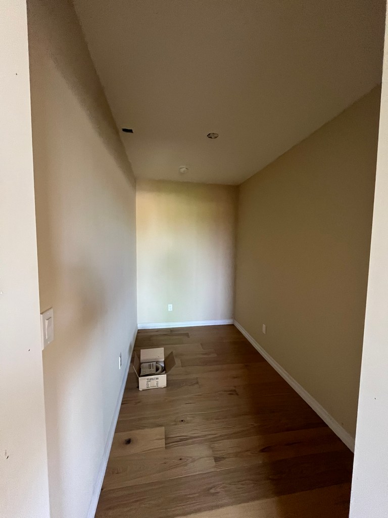 Narrow hallway with hardwood flooring, painted walls, baseboards, and ceiling fixture openings.
