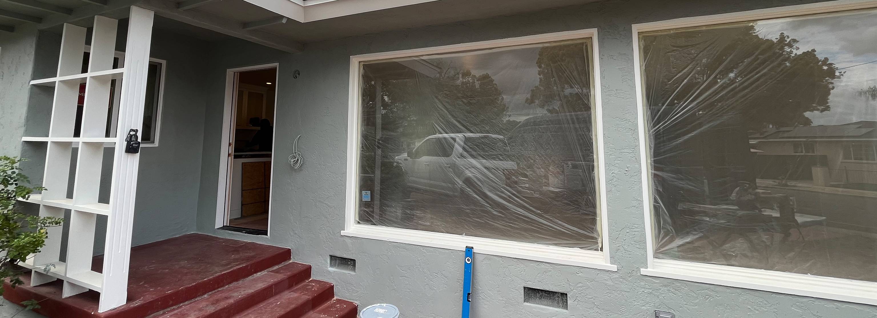 Exterior shows covered windows, red-painted entry steps, and a modern vertical lattice accent near the front door.
