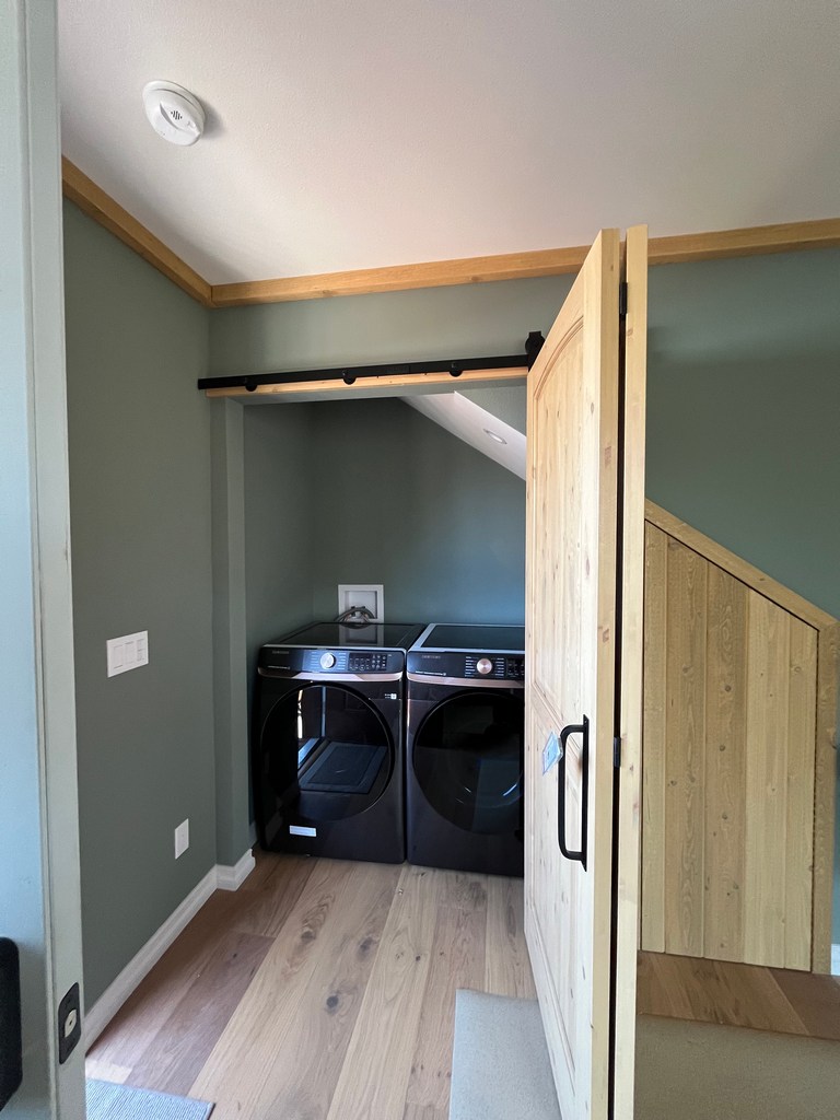 Laundry alcove with sliding wood barn door, appliances, hardwood floor, and painted walls.