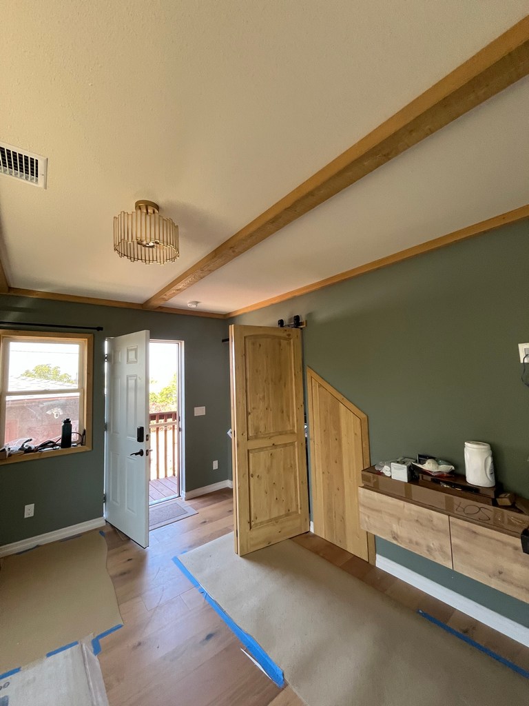 Finished interior room with wood trim, barn door, stair paneling, hardwood floor, and open exterior door.