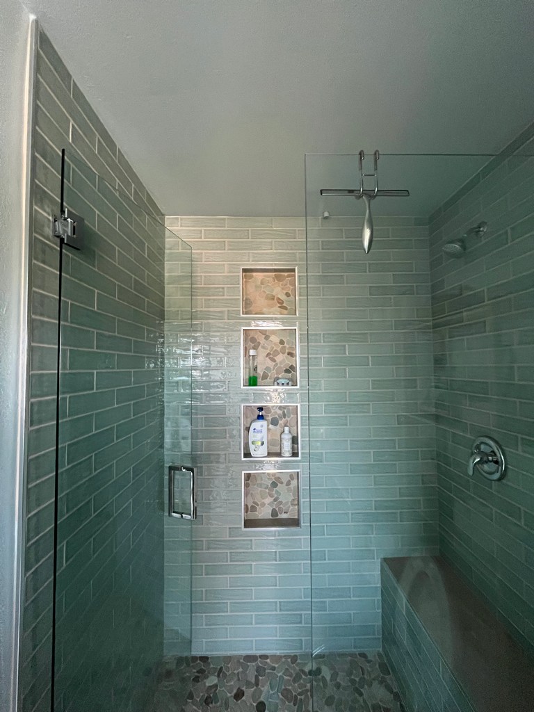 Finished shower with green subway tile, glass enclosure, pebble floor, niches, and bench.